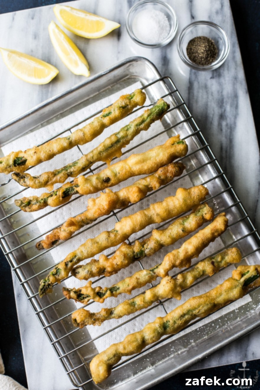Overhead photo of asparagus tempura on a rack on a silver tray