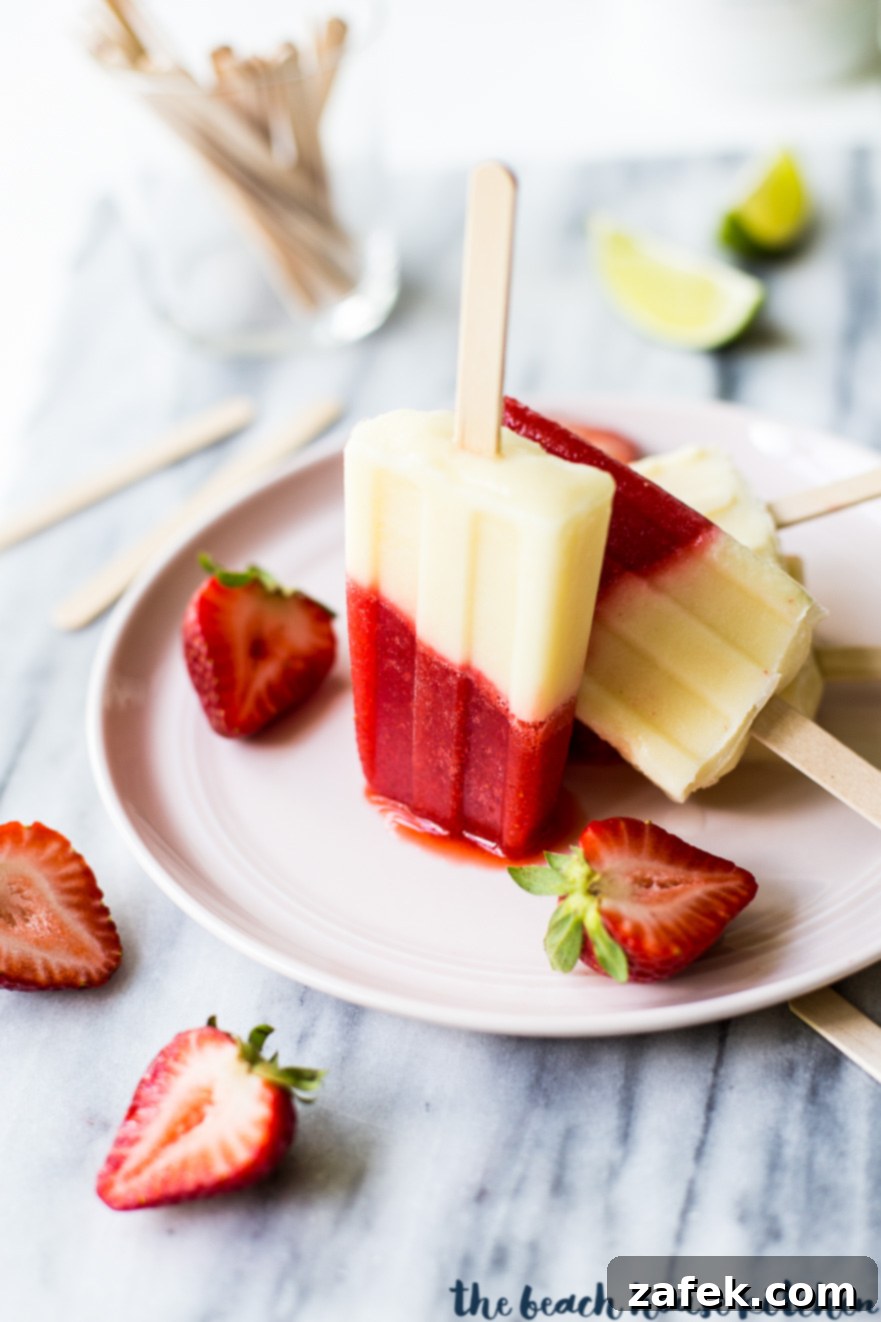 Miami Vice Boozy Popsicles on a pink plate surrounded by a few halved strawberries