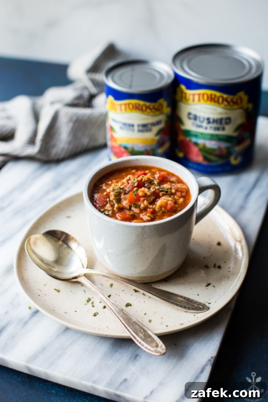 A mug of stuffed pepper soup on a plate with two spoons