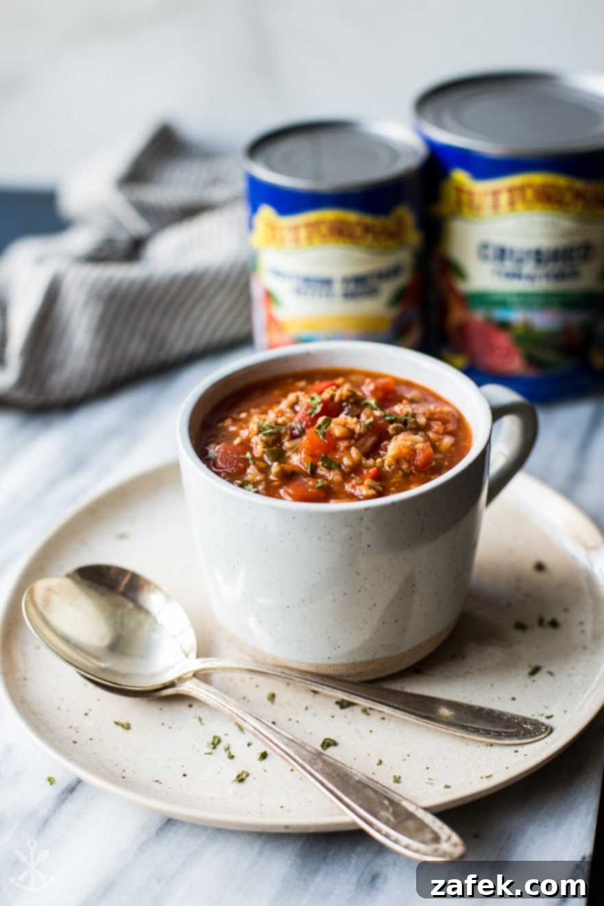 A mug of stuffed pepper soup on a plate with two spoons