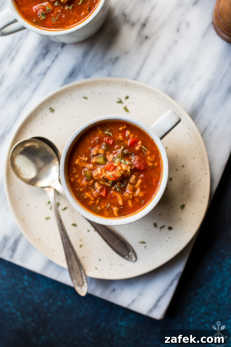 Overhead up close photo of a mug of stuffed pepper soup on a plate with two spoons