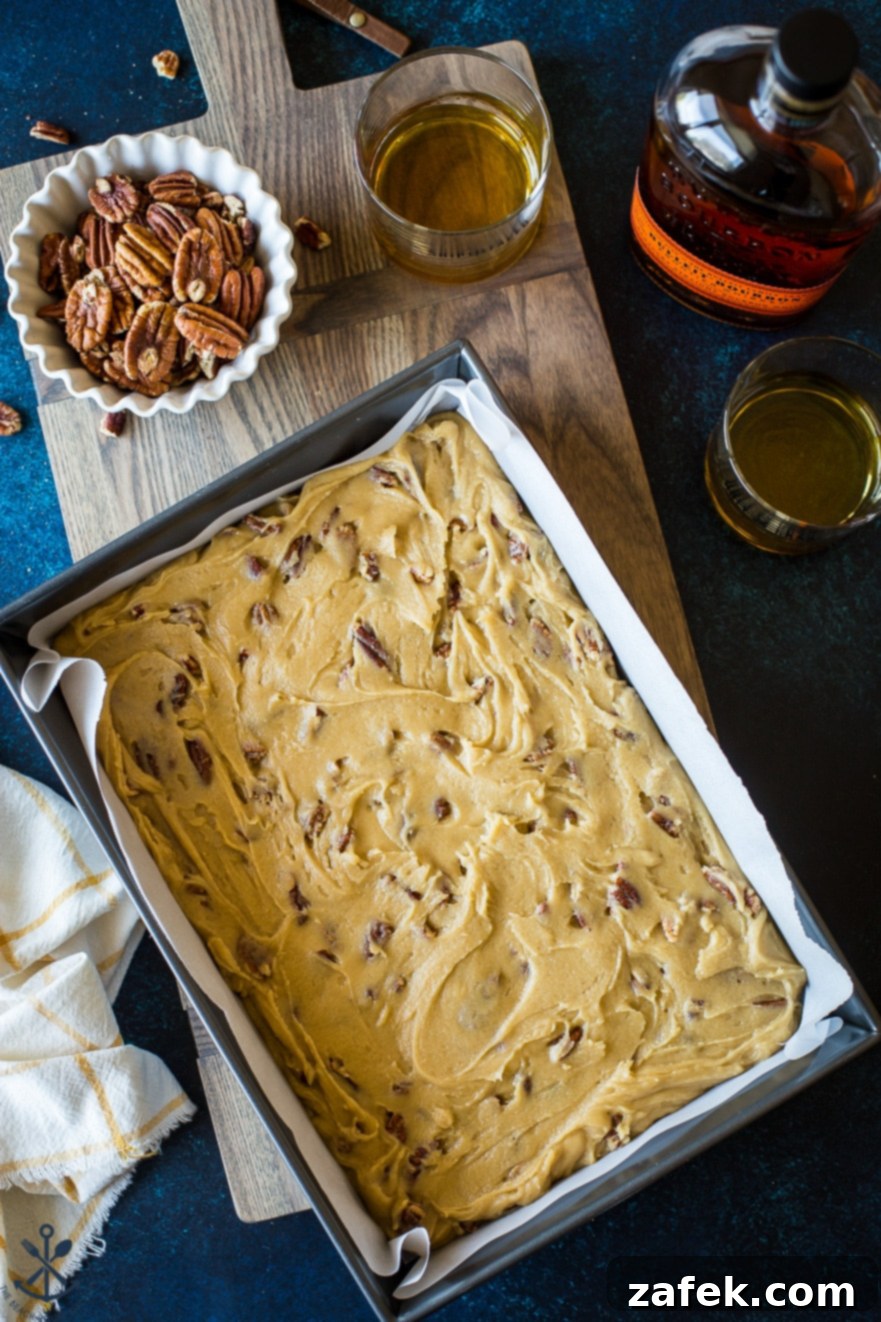 Overhead photo of the unbaked pecan bourbon blondie batter, topped with extra pecans before going into the oven.