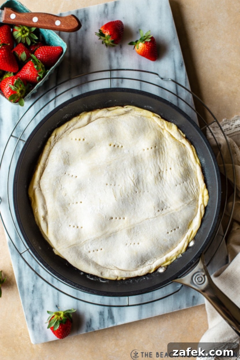 Blushing Strawberry Caramel Tart 6 Overhead photo of a pre-baked tarte tatin in a cast iron skillet, with puff pastry covering the fruit layer.