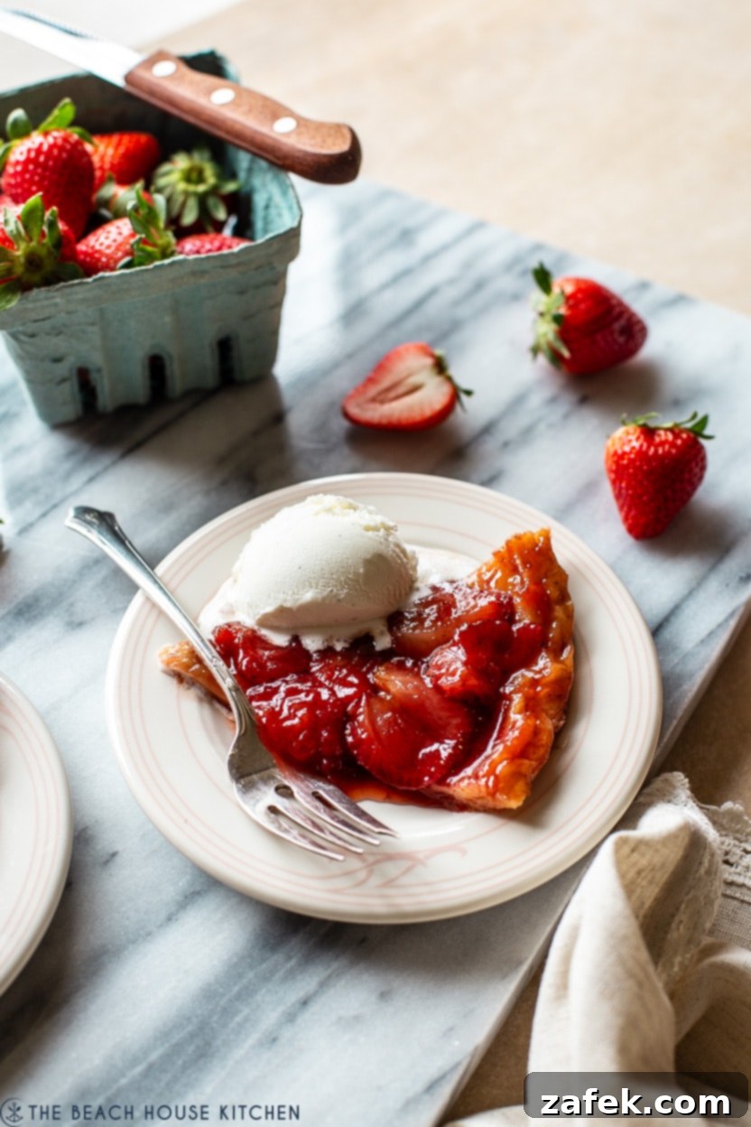 Blushing Strawberry Caramel Tart 7 A photo of a single slice of strawberry tarte tatin on a white plate, garnished with a sprig of mint and served with a scoop of vanilla ice cream.