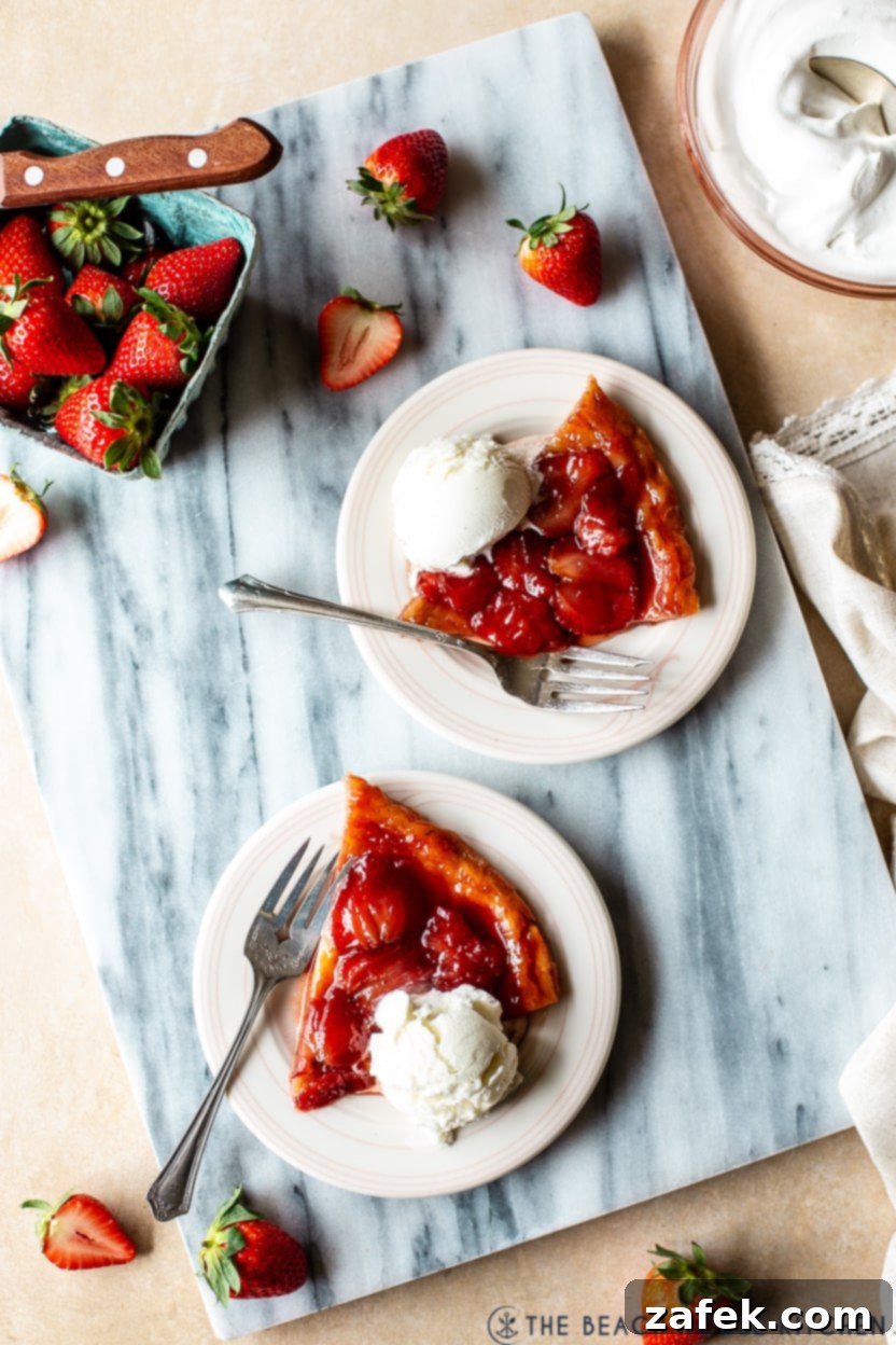 Blushing Strawberry Caramel Tart 8 Overhead photo of two slices of strawberry tarte tatin on small white plates, each with a scoop of vanilla ice cream, ready to be served.