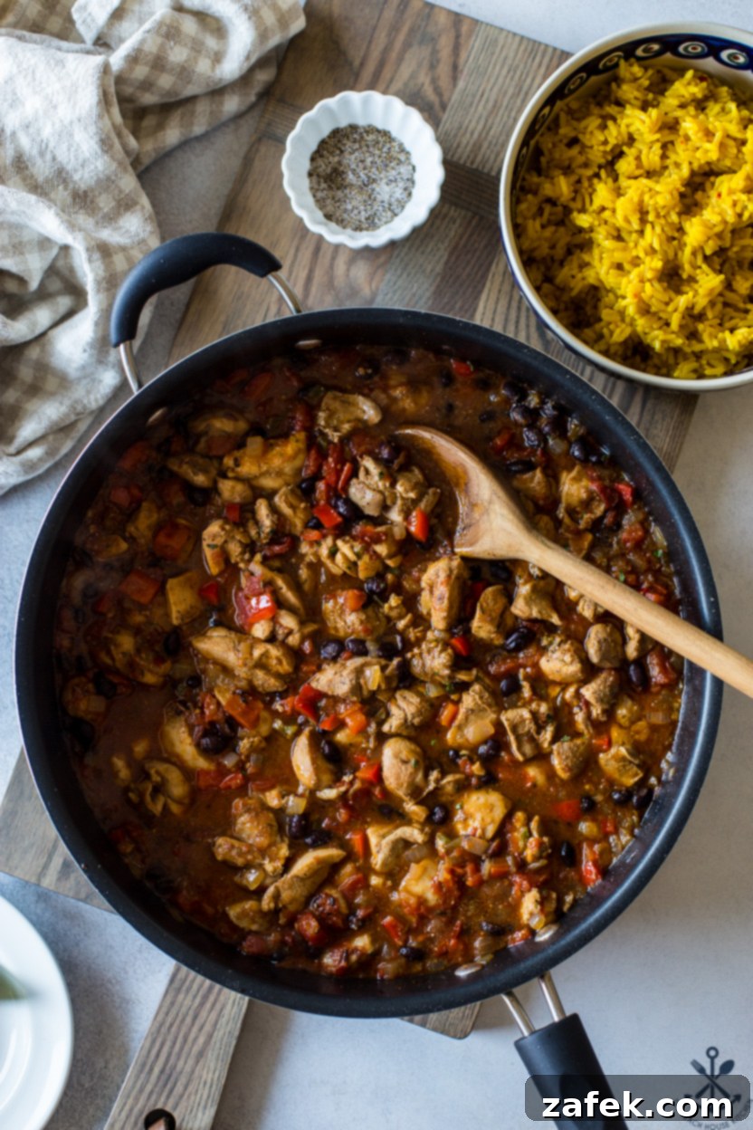 Overhead photo of a skillet of Cuban spiced chicken, rice, black beans, and colorful veggies