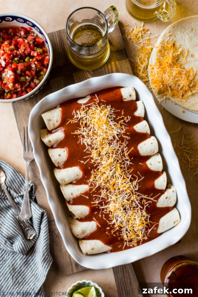 Effortless Homemade Beef Enchiladas 7 Overhead photo of a pan of pre-baked enchiladas topped with enchilada sauce and shredded cheese