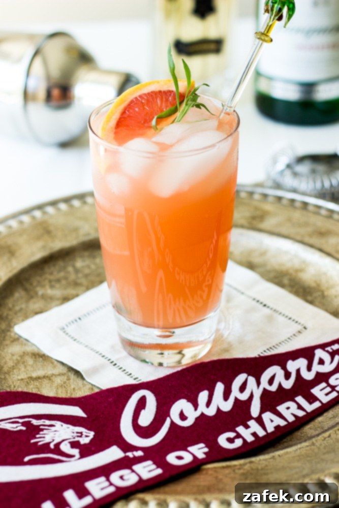 The Charleston Sparkle 2 A sparkling Charleston Fizz cocktail in a tall glass, garnished with a grapefruit slice and fresh tarragon.