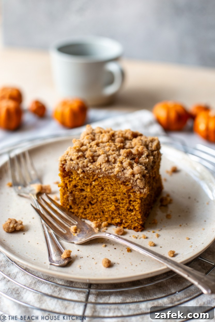Slice of pumpkin crumb snack cake on a plate with two forks, showing the moist interior and crumb topping