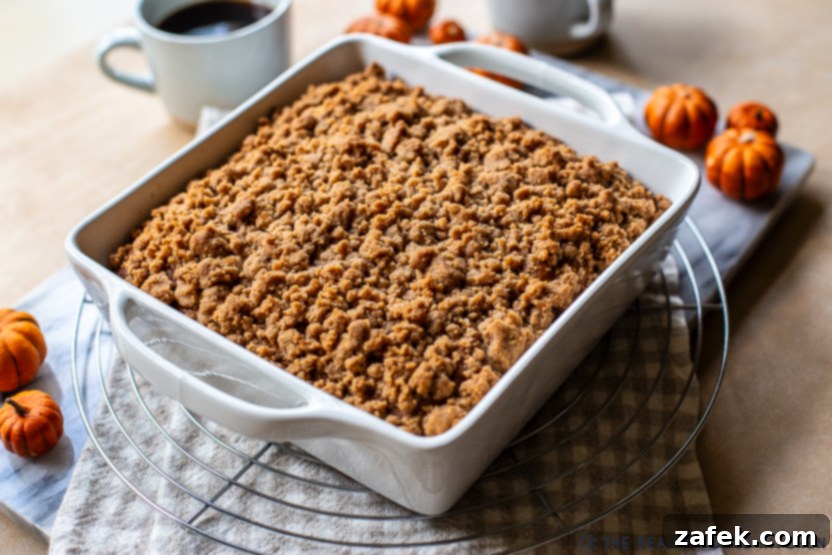 A photo of a pumpkin crumb snack cake in a white dish on a wire rack, cooling after baking