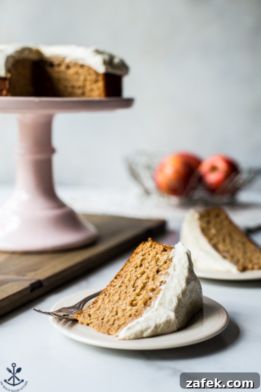 A beautifully sliced Applesauce Cake with rich Vanilla Bean Frosting presented on a plate, with the full cake on a stand in the background, ready for serving.