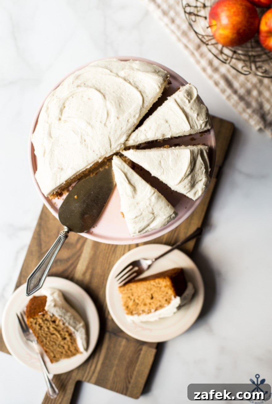 An inviting overhead photo of a whole Applesauce Cake with Vanilla Bean Frosting resting on a rustic wooden board, flanked by two perfectly sliced portions on individual plates, ready to be enjoyed.