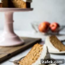 A slice of applesauce cake with vanilla bean frosting a a plate with a cake stand in background