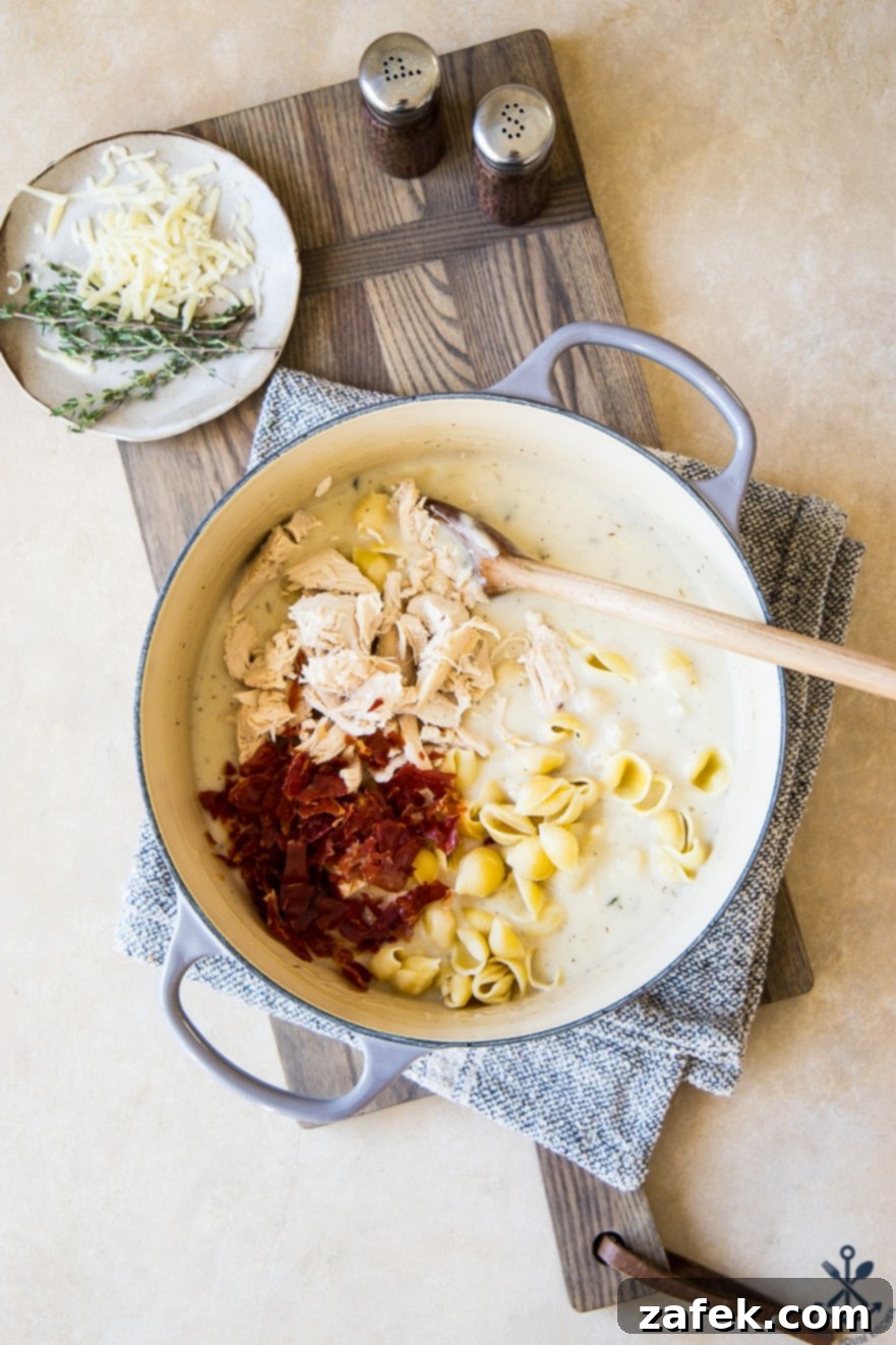 Creamy Cordon Bleu Chicken Pasta Bake 6 Various ingredients for the pasta bake laid out in a large pot before mixing, including cooked pasta, shredded chicken, and crispy prosciutto.
