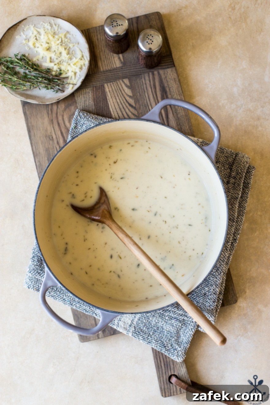 Creamy Cordon Bleu Chicken Pasta Bake 7 A wooden spoon stirring a creamy, golden sauce in a large pot, showing the smooth consistency of the sauce.