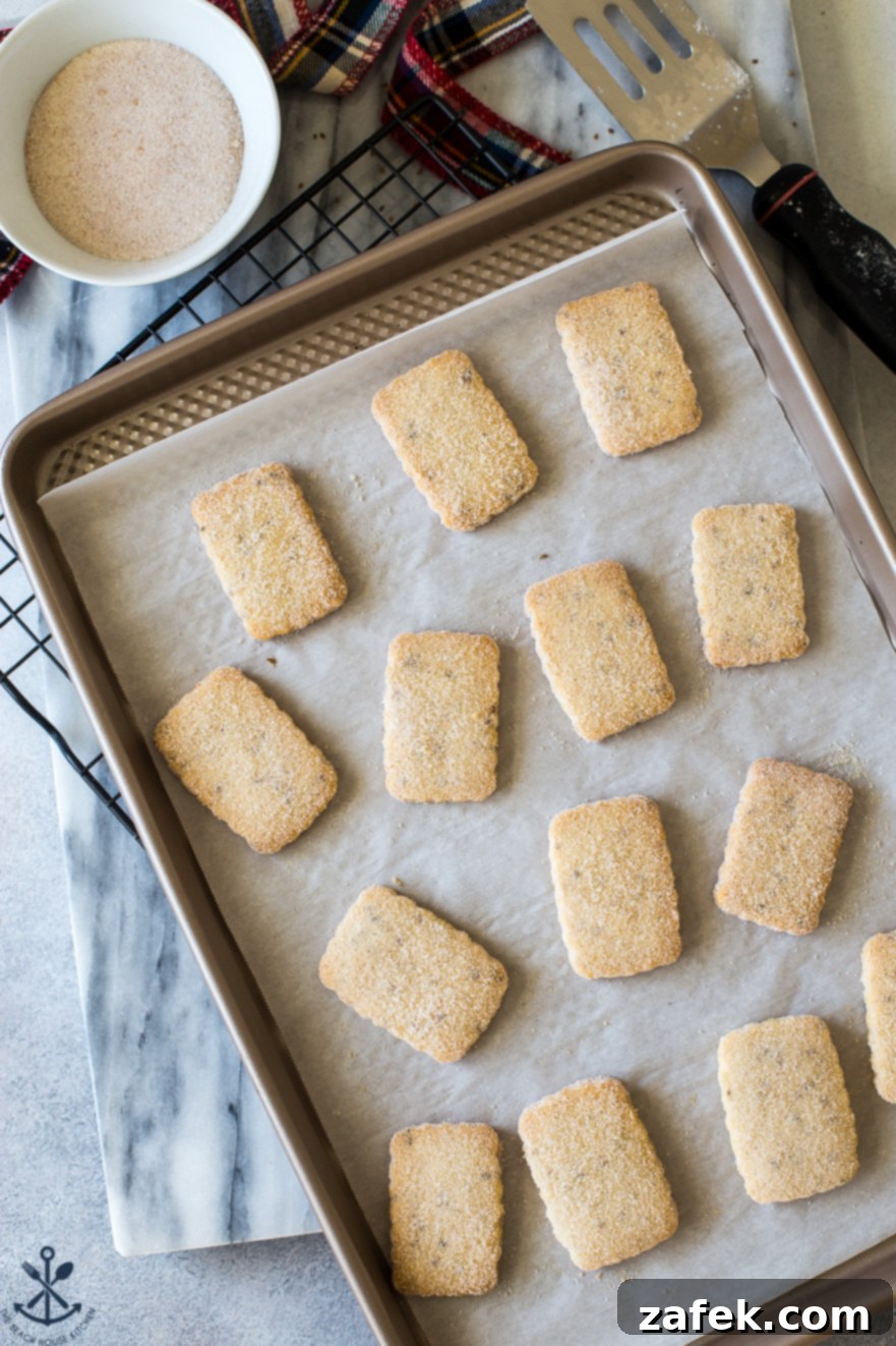 An array of Biscochitos cookies, uniformly baked to a light golden hue, arranged neatly on a gleaming gold baking sheet, highlighting their delicate texture.