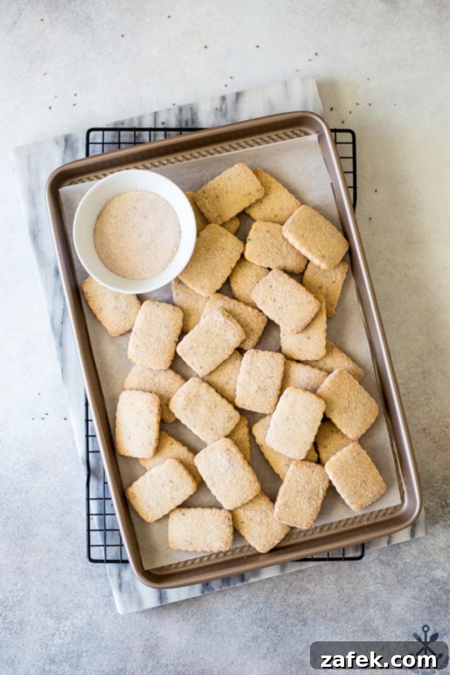 Rows of freshly baked Biscochitos cookies, featuring their appealing golden-brown edges and cinnamon sugar dusting, displayed on a gold baking sheet.