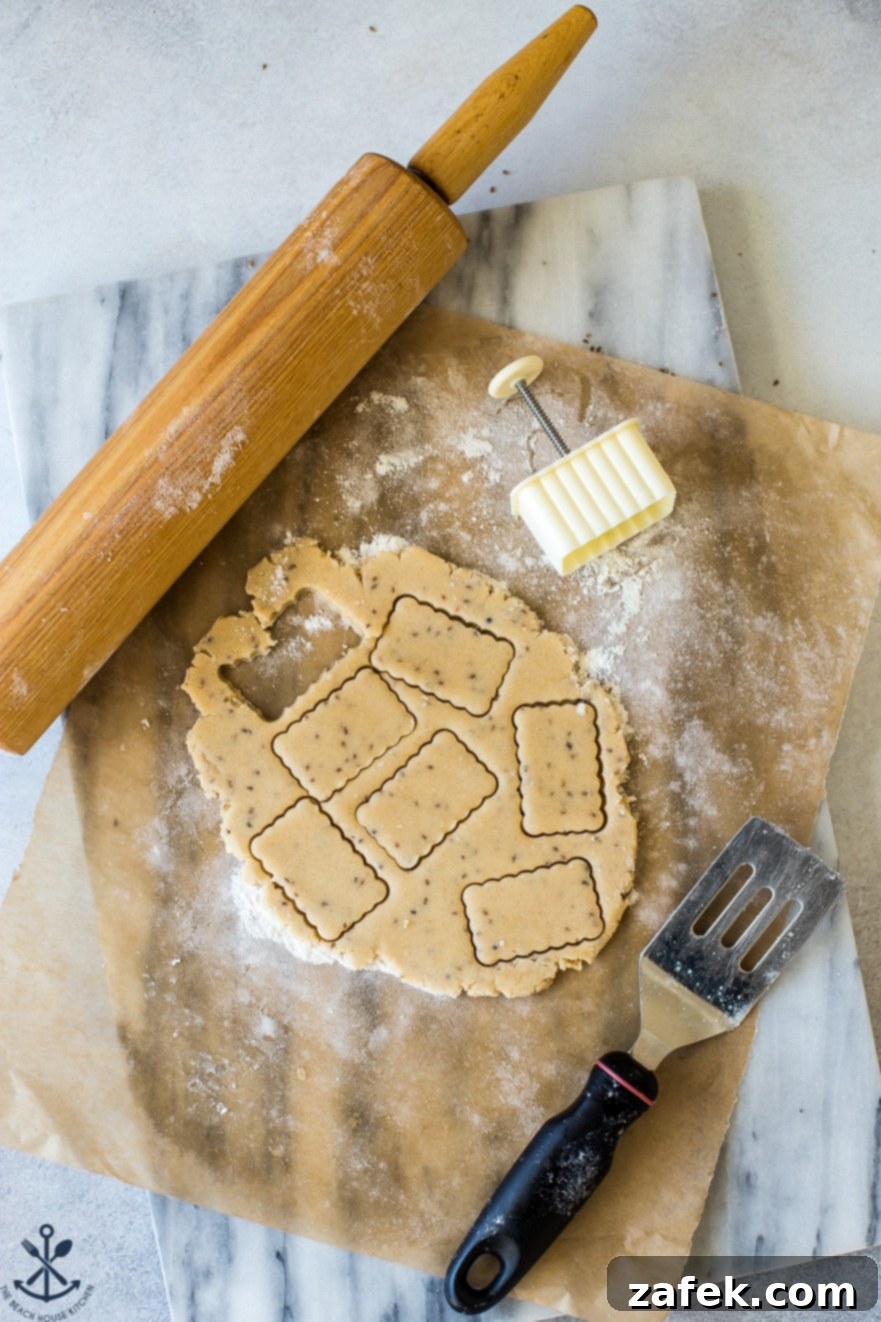 Unbaked Biscochitos dough, perfectly rolled out and shaped into traditional designs, rests on a pristine marble board next to a rolling pin, showcasing the preparation stage.