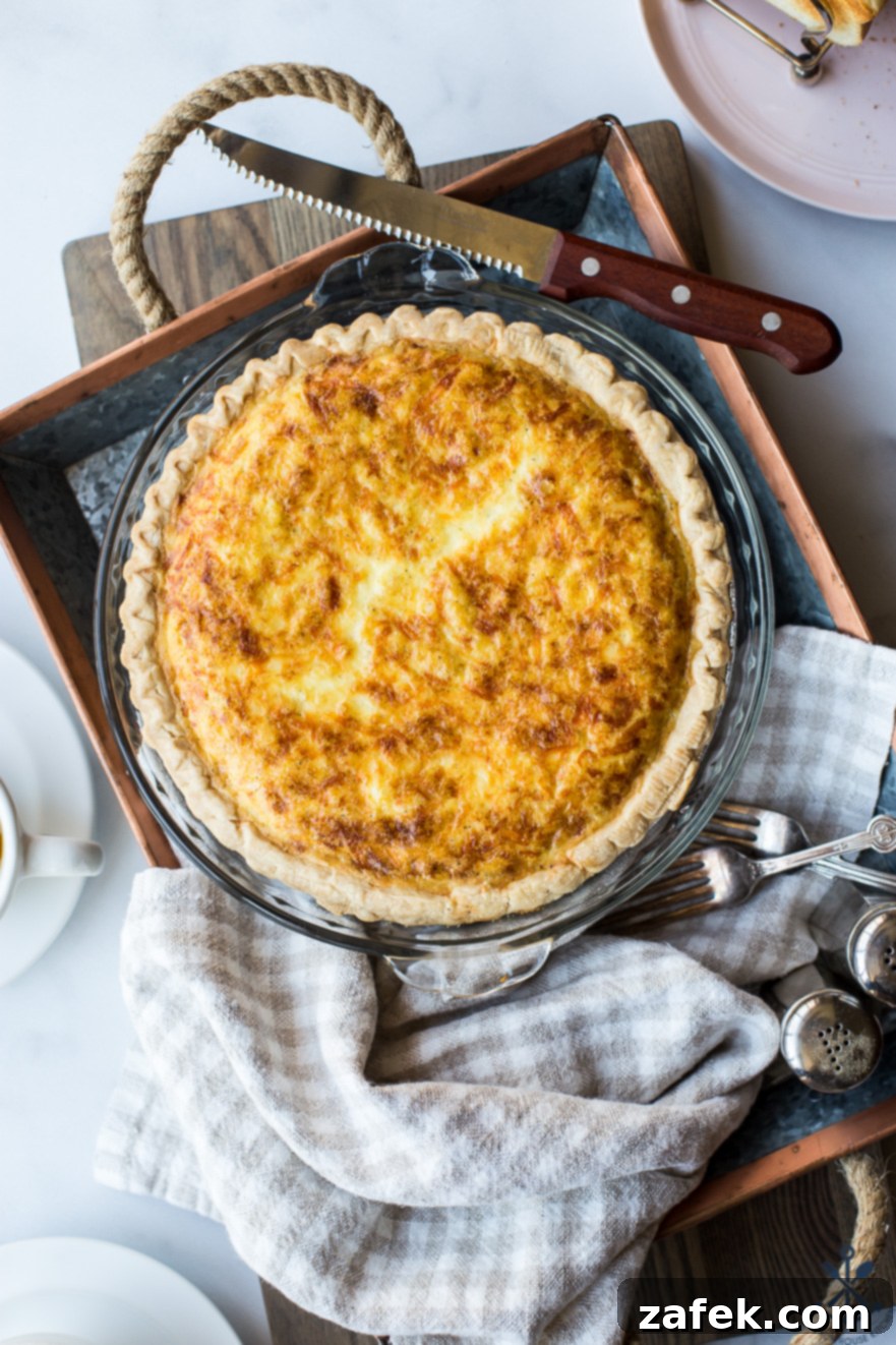 Overhead photo of quiche lorraine in a pie plate on a silver tray, perfectly baked and golden