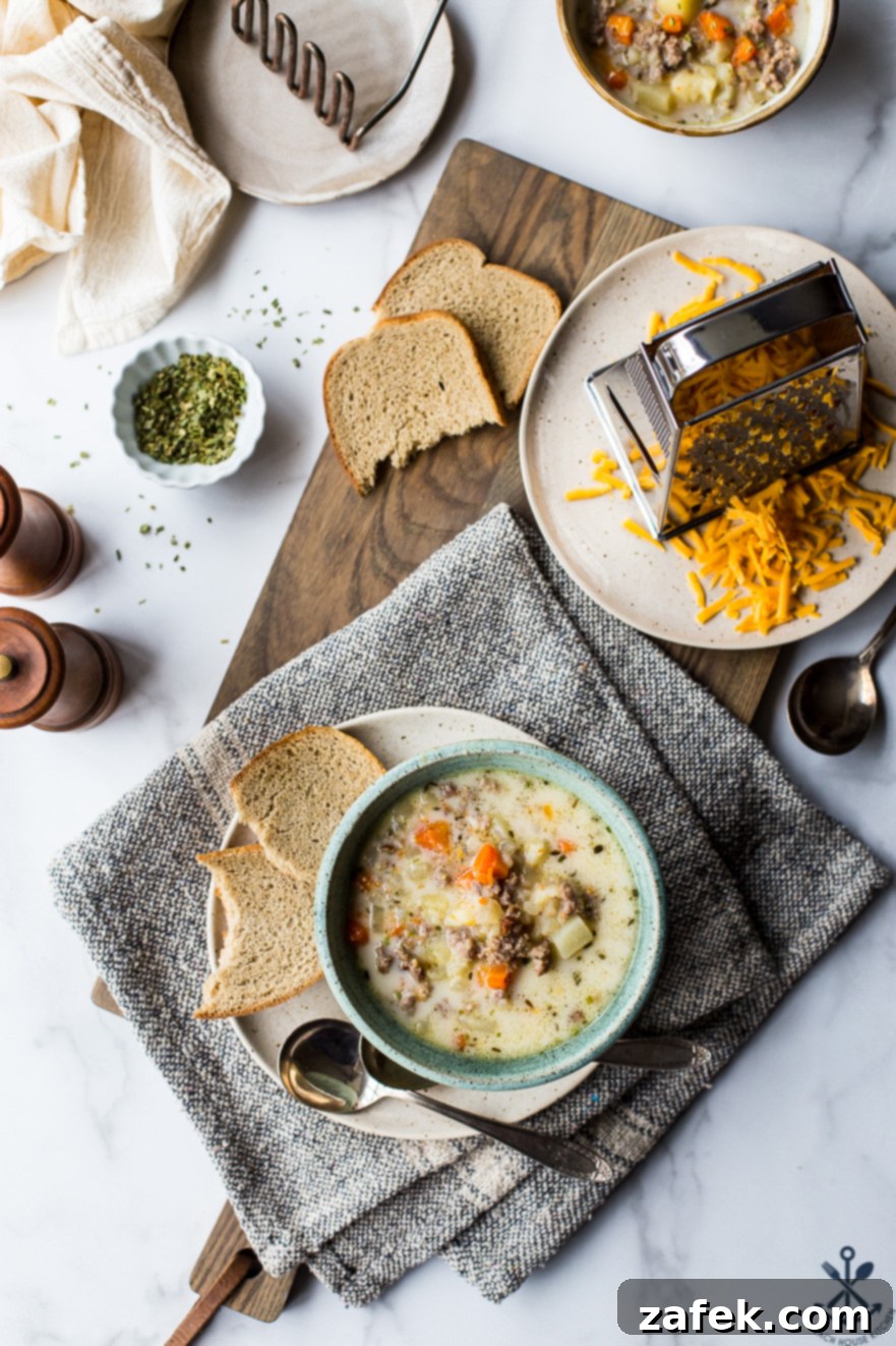 Overhead photo of a bowl of slow cooker bratwurst potato soup in a bowl on a plate with some bread and a spoon