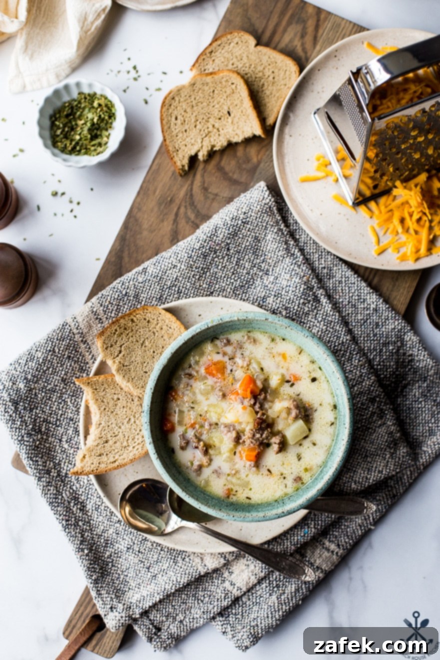 Overhead photo of a bowl of slow cooker bratwurst potato soup in a bowl on a plate with some bread and a spoon, garnished perfectly