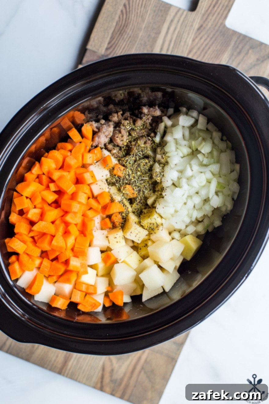 Overhead photo of a slow cooker filled with carrots, potatoes, onions, and browned bratwurst, ready to cook