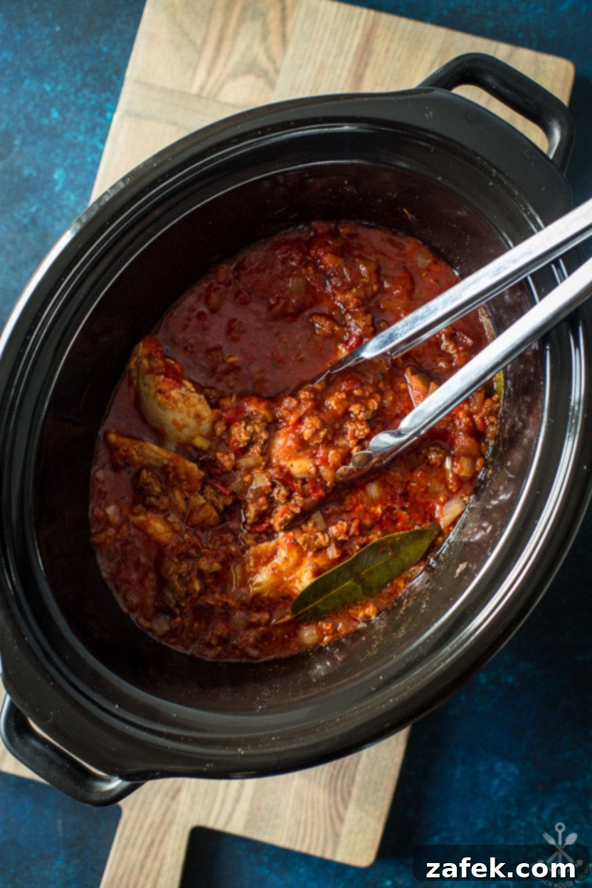 Overhead photo of a slow cooker filled with finished chicken tinga, bubbling gently
