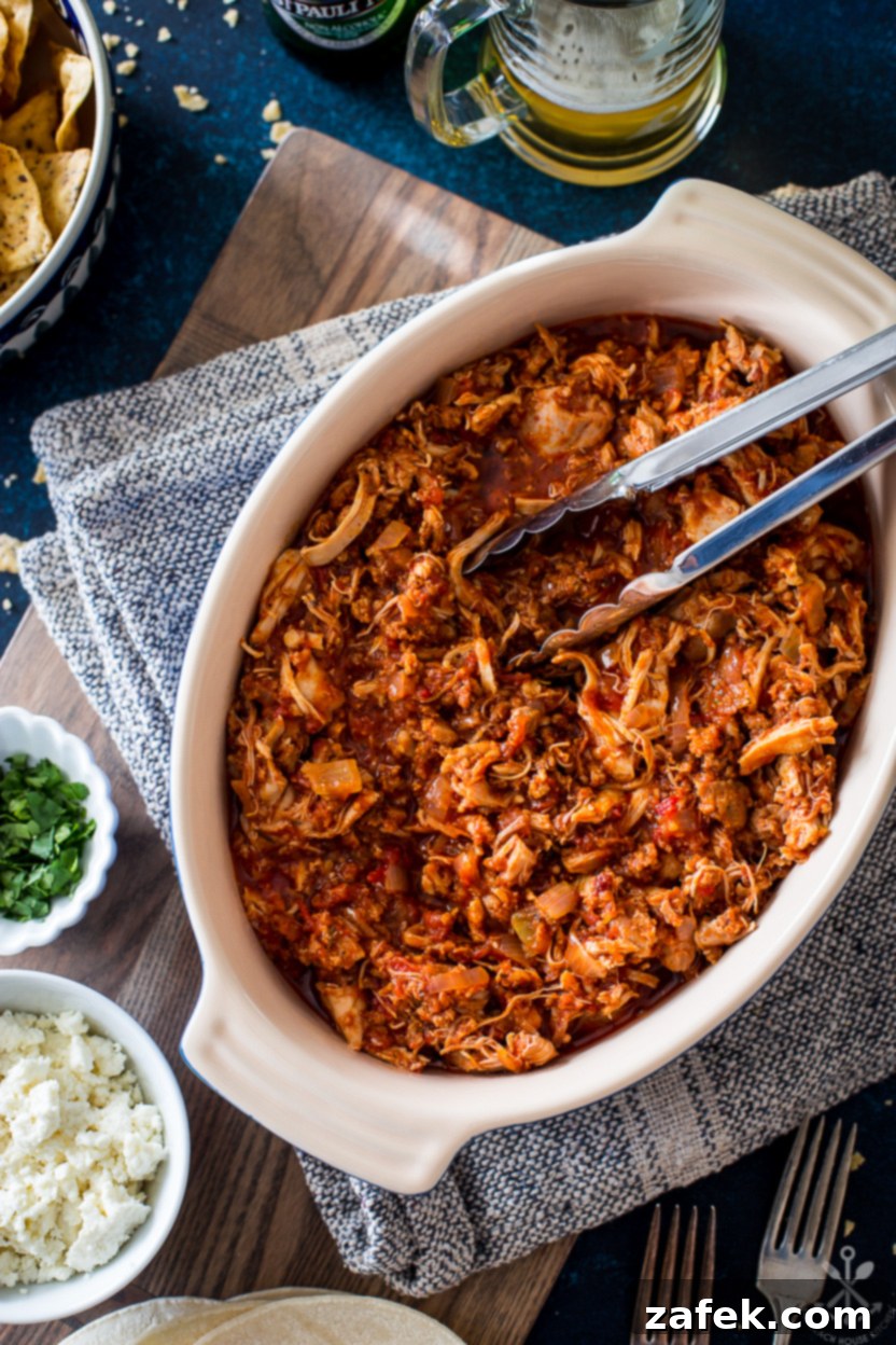 Overhead photo of an oval dish of chicken tinga garnished with fresh cilantro and lime wedges