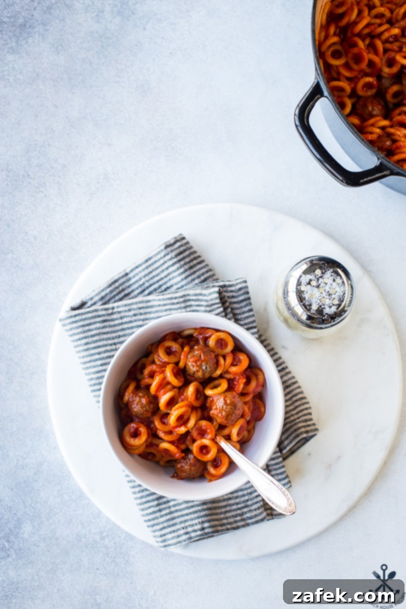 Overhead photo of a bowl of homemade SpaghettiO's on a round marble board with a Parmesan cheese shaker nearby