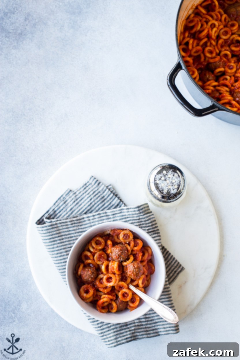 Overhead photo of a bowl of homemade SpaghettiO's on a round marble board, with a pot of SpaghettiO's off to the side
