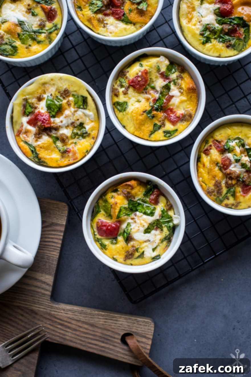 Overhead photo of savory sausage, tomato, spinach, and mozzarella egg cups freshly baked on a cookie sheet, ready for meal prep