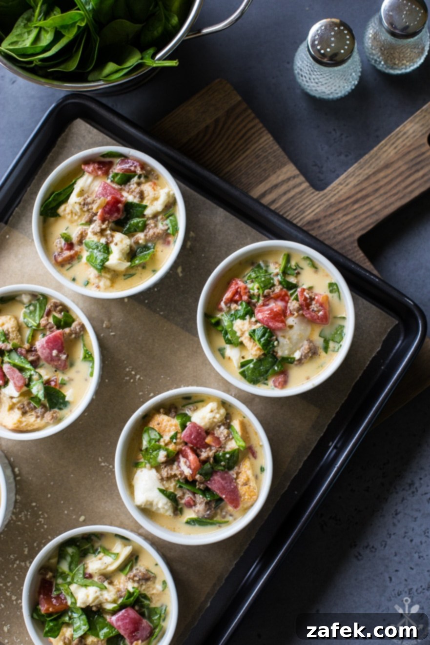 Unbaked sausage, tomato, spinach, and mozzarella egg cup mixture meticulously scooped into individual ramekins, arranged on a parchment-lined baking sheet, awaiting their entry into the preheated oven