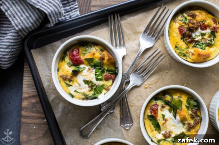 A baking tray showcasing several golden-brown baked sausage, tomato, spinach, and mozzarella egg cups, served with three gleaming silver forks, emphasizing their readiness to be savored as a wholesome and appealing breakfast or light meal