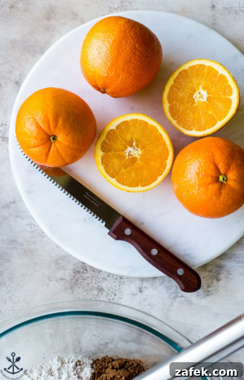 Zesty Chocolate Orange Bundt 4 Fresh, vibrant oranges on a marble circular board with a sharp knife, ready for zest and juice.
