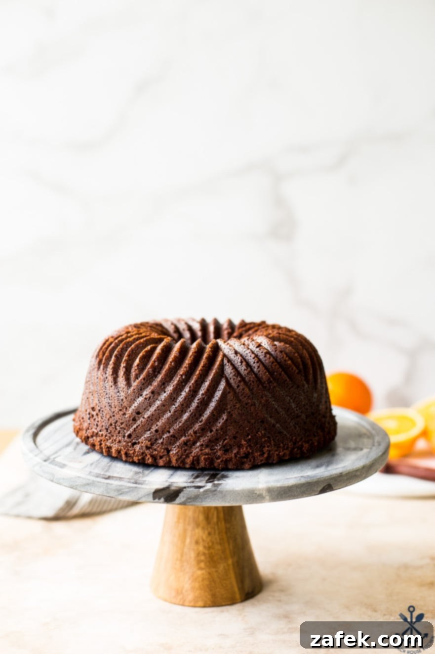 Zesty Chocolate Orange Bundt 5 A majestic chocolate orange bundt cake resting on a cake stand with a warm wooden base, ready to be served.