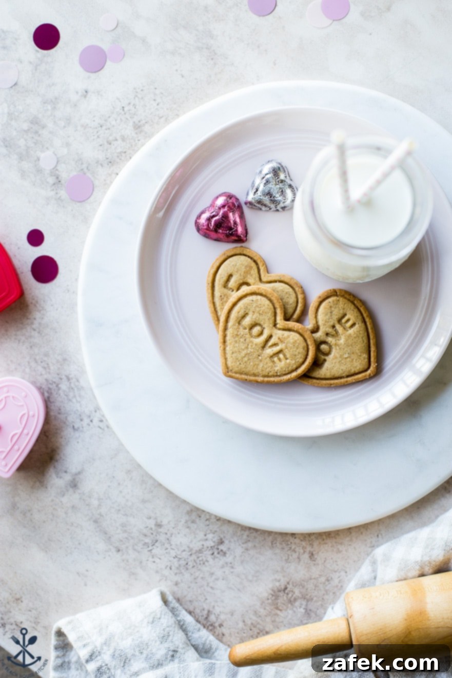 Brown Butter Honey Cardamom Delights 2 A trio of heart-shaped Brown Butter Honey Cardamom Cookies, elegantly imprinted with 'LOVE', resting on a white plate beside a charming bottle of milk. The perfect homemade Valentine's Day treat.
