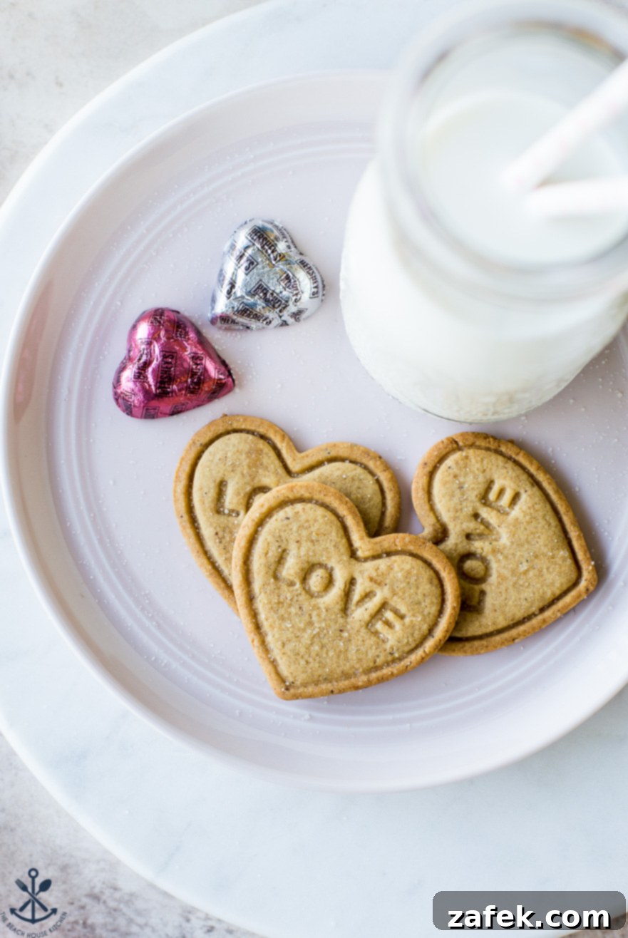 Brown Butter Honey Cardamom Delights 3 Three perfectly baked heart-shaped Brown Butter Honey Cardamom Cookies, each intricately embossed with 'LOVE', arranged artfully on a white plate with a whimsical mini milk bottle, ready for a romantic celebration.