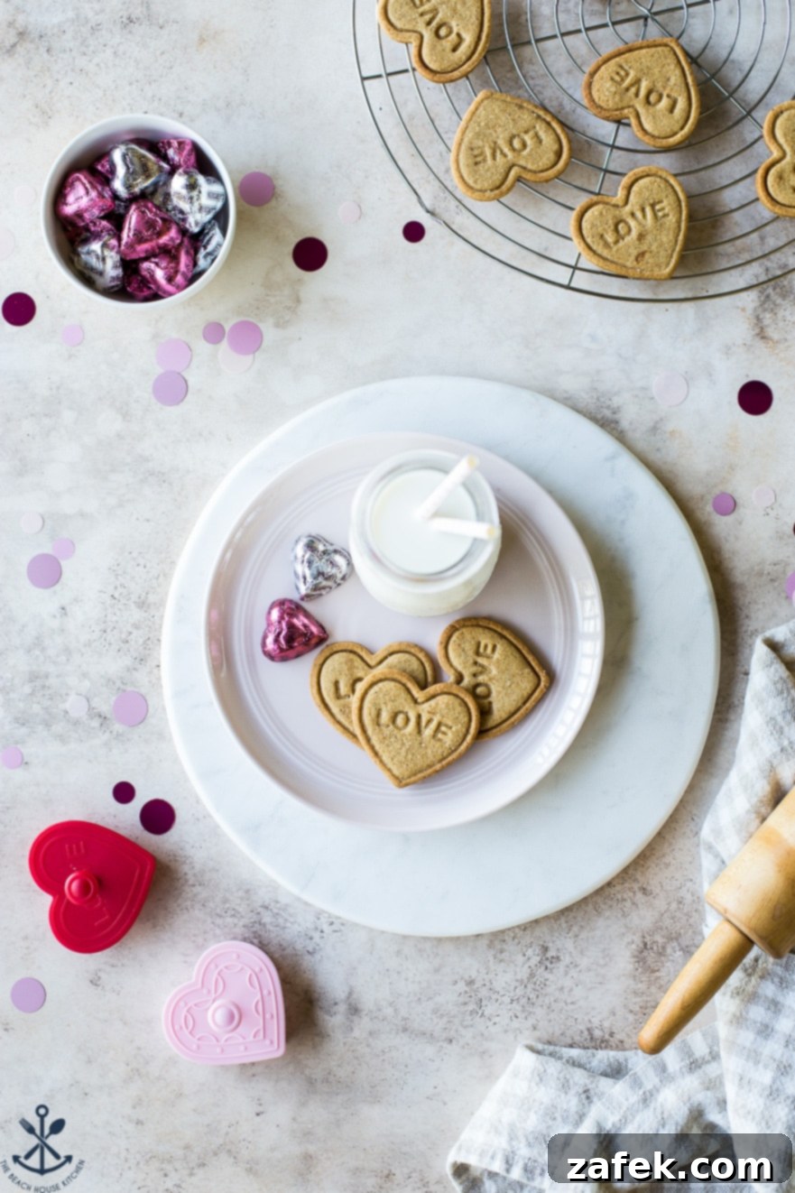 Brown Butter Honey Cardamom Delights 6 Three golden brown, heart-shaped cookies, each lovingly embossed with 'LOVE', presented on a pristine white plate, accompanied by a small bottle of milk, embodying a perfect, cozy Valentine's Day treat.