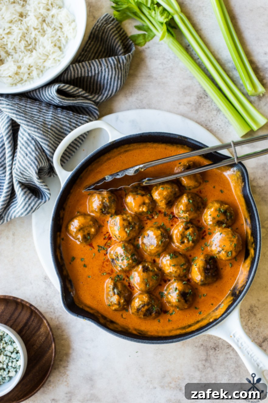 Close-up overhead photo of buffalo turkey meatballs simmering in a vibrant red sauce in a white skillet.