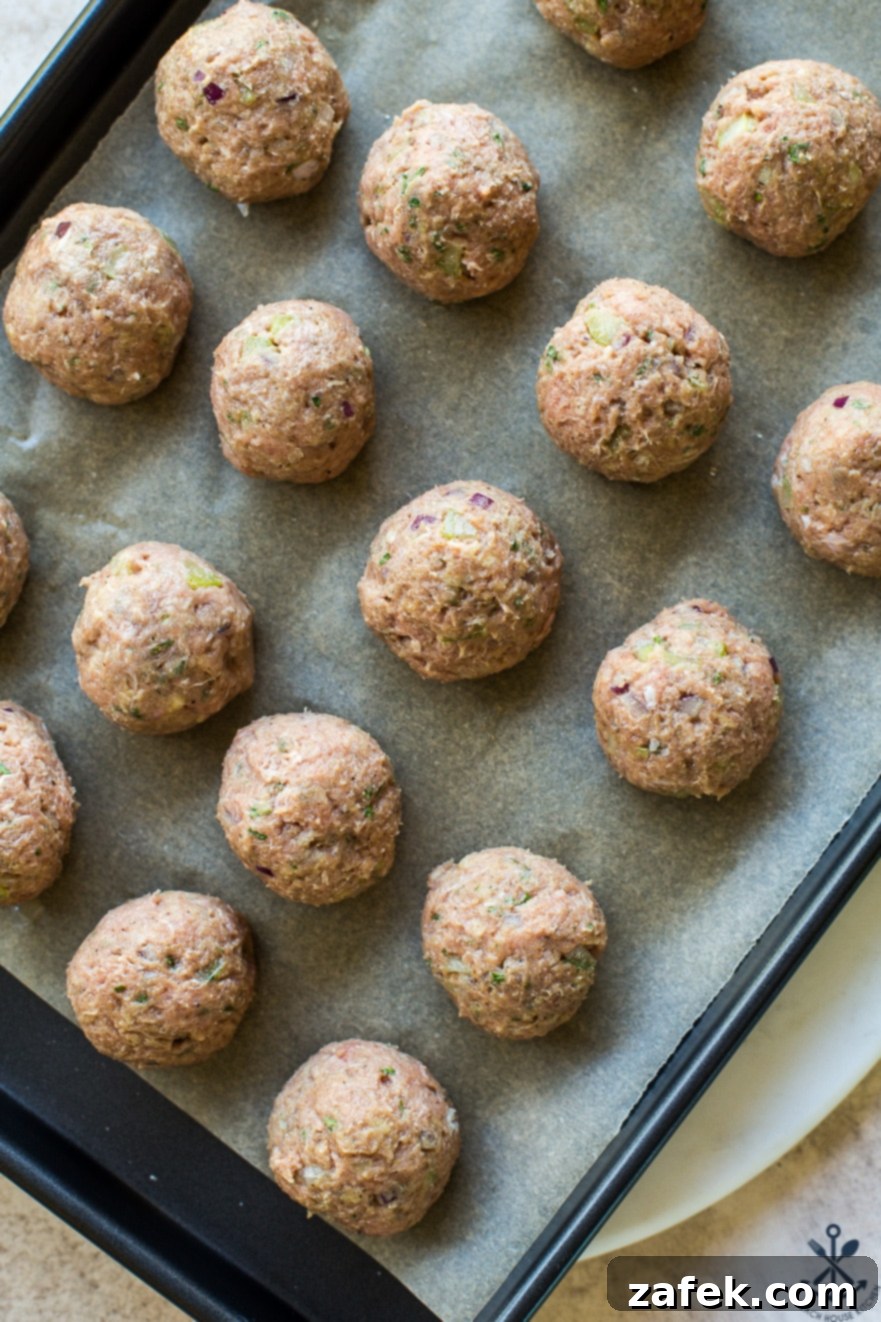 Overhead photo of pre-cooked buffalo turkey meatballs arranged neatly on a baking sheet lined with parchment paper, before being sauced.