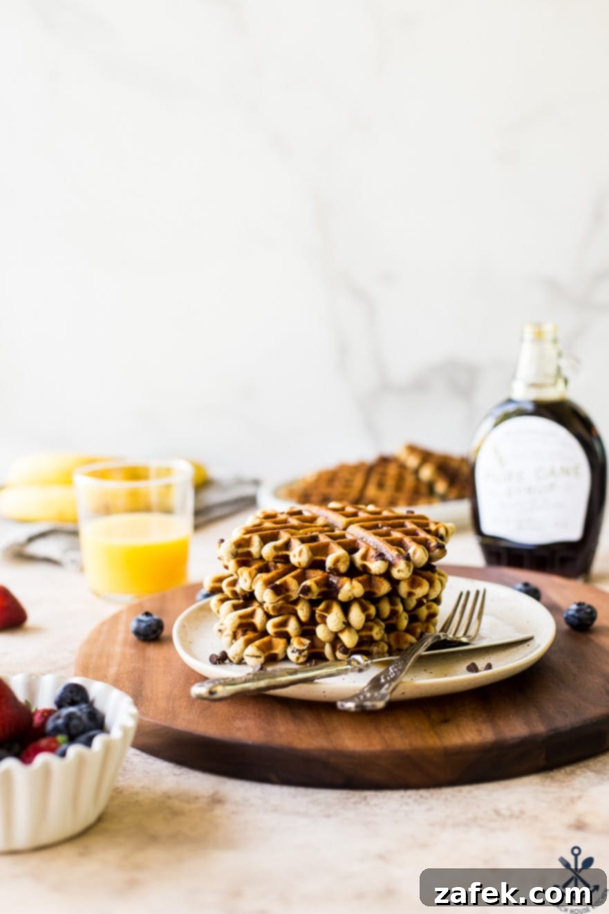 Ultimate Chocolate Chip Banana Bread Waffles 3 A close-up view of chocolate chip banana bread waffles piled high on a white plate, served on a warm wooden serving board, ready to be enjoyed.