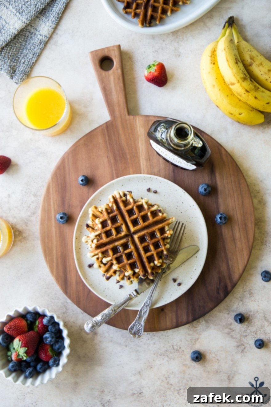 Ultimate Chocolate Chip Banana Bread Waffles 4 An inviting overhead shot of three chocolate chip banana bread waffles stacked on a white plate, served on a rustic wooden board, garnished with powdered sugar and a sprig of mint.