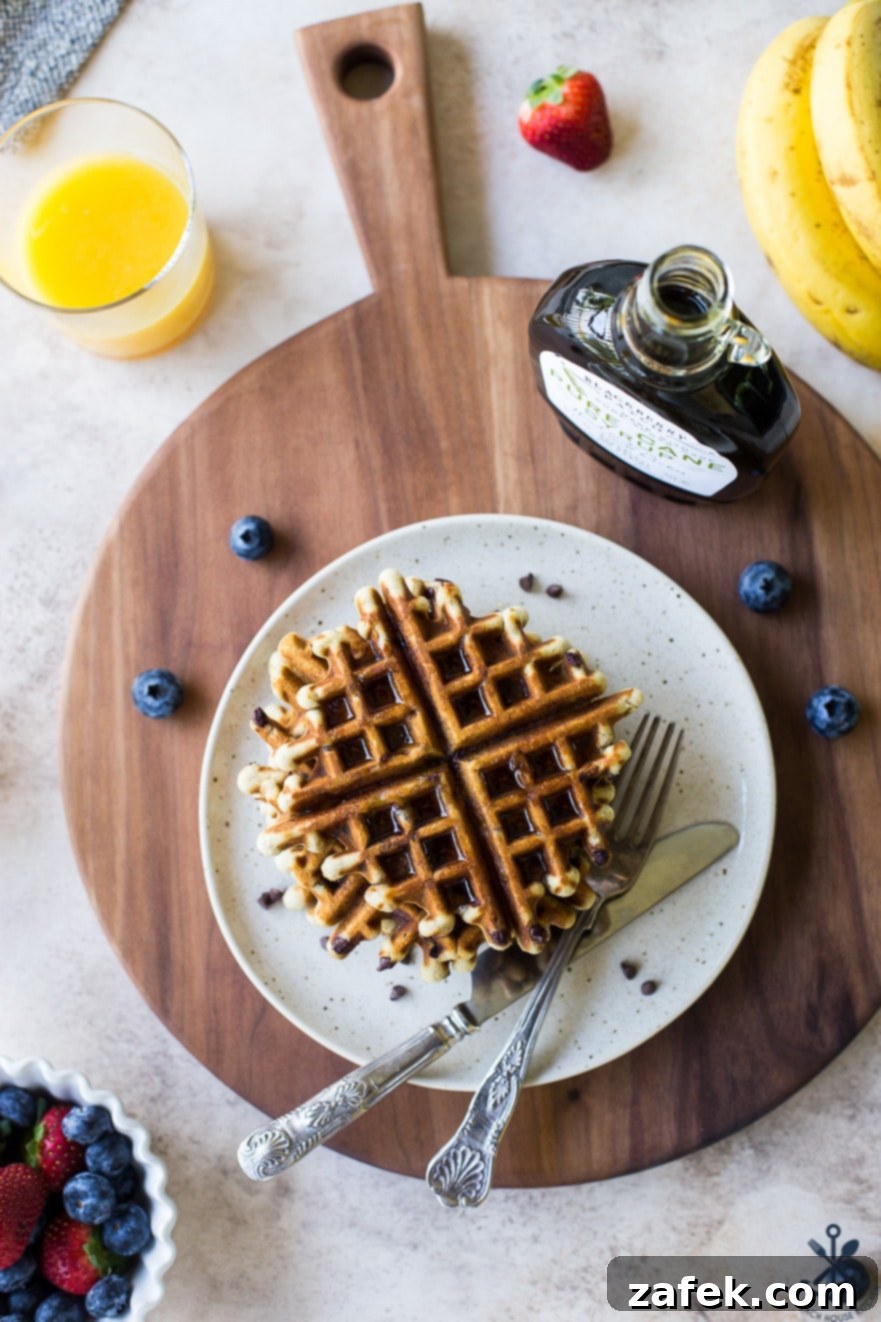 Ultimate Chocolate Chip Banana Bread Waffles 5 Overhead photo showing a beautifully arranged plate of chocolate chip banana bread waffles with fresh berries and syrup, presented on a rich, dark wooden board, highlighting the artisanal quality of the serving ware.