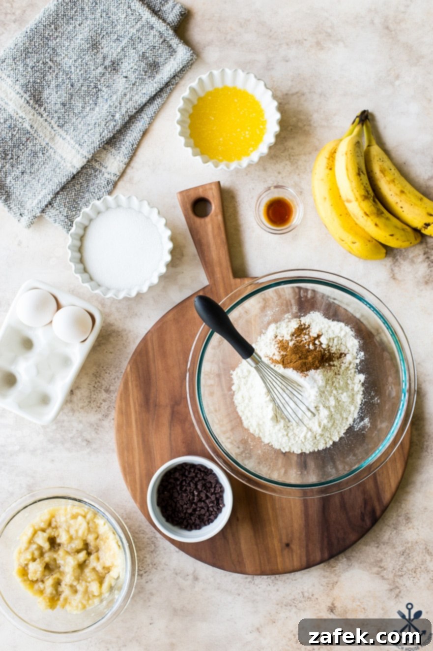 Ultimate Chocolate Chip Banana Bread Waffles 6 A beautiful flat lay of all the dry and wet ingredients for chocolate chip banana bread waffles laid out in various bowls on a large, intricately grained wooden board, showcasing both the recipe's simplicity and the board's aesthetic.