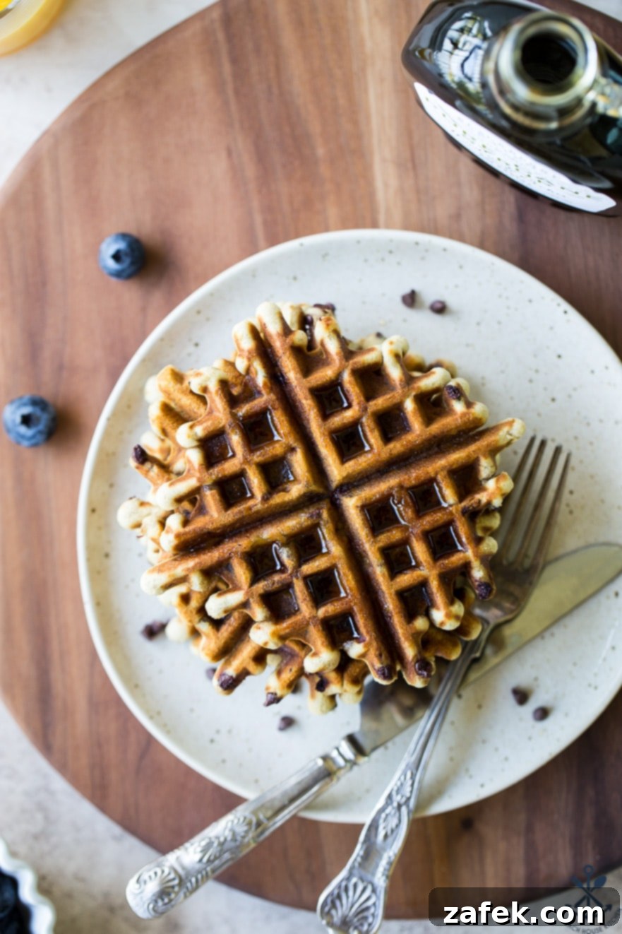 Ultimate Chocolate Chip Banana Bread Waffles 7 Another overhead shot showcasing golden-brown chocolate chip banana bread waffles on a pristine white plate atop a dark wooden serving board, emphasizing their appetizing texture and golden hue.
