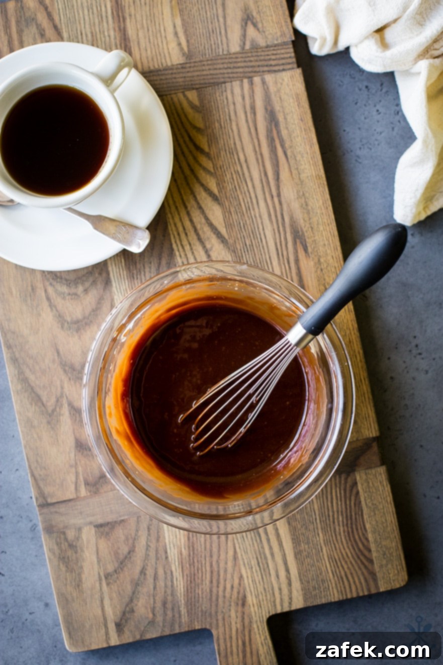 Baked Mocha Donuts 7 Rich mocha glaze in a clear glass bowl, with a whisk and a cup of freshly brewed coffee nearby, ready for dipping.