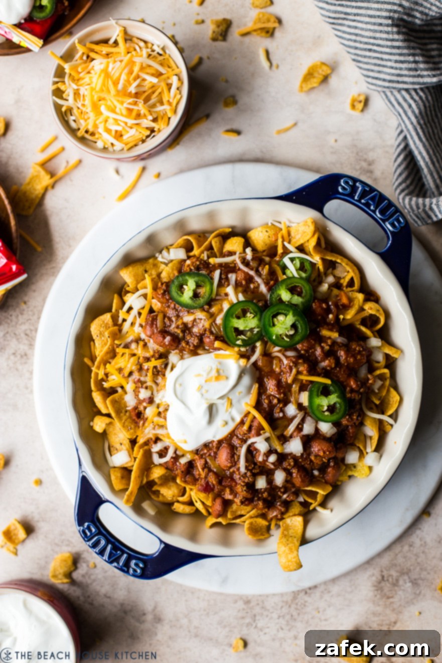 Overhead photo of a round blue baking dish filled with a generous serving of Frito Pie, showcasing a golden-brown cheesy top over a rich chili base with crunchy corn chips