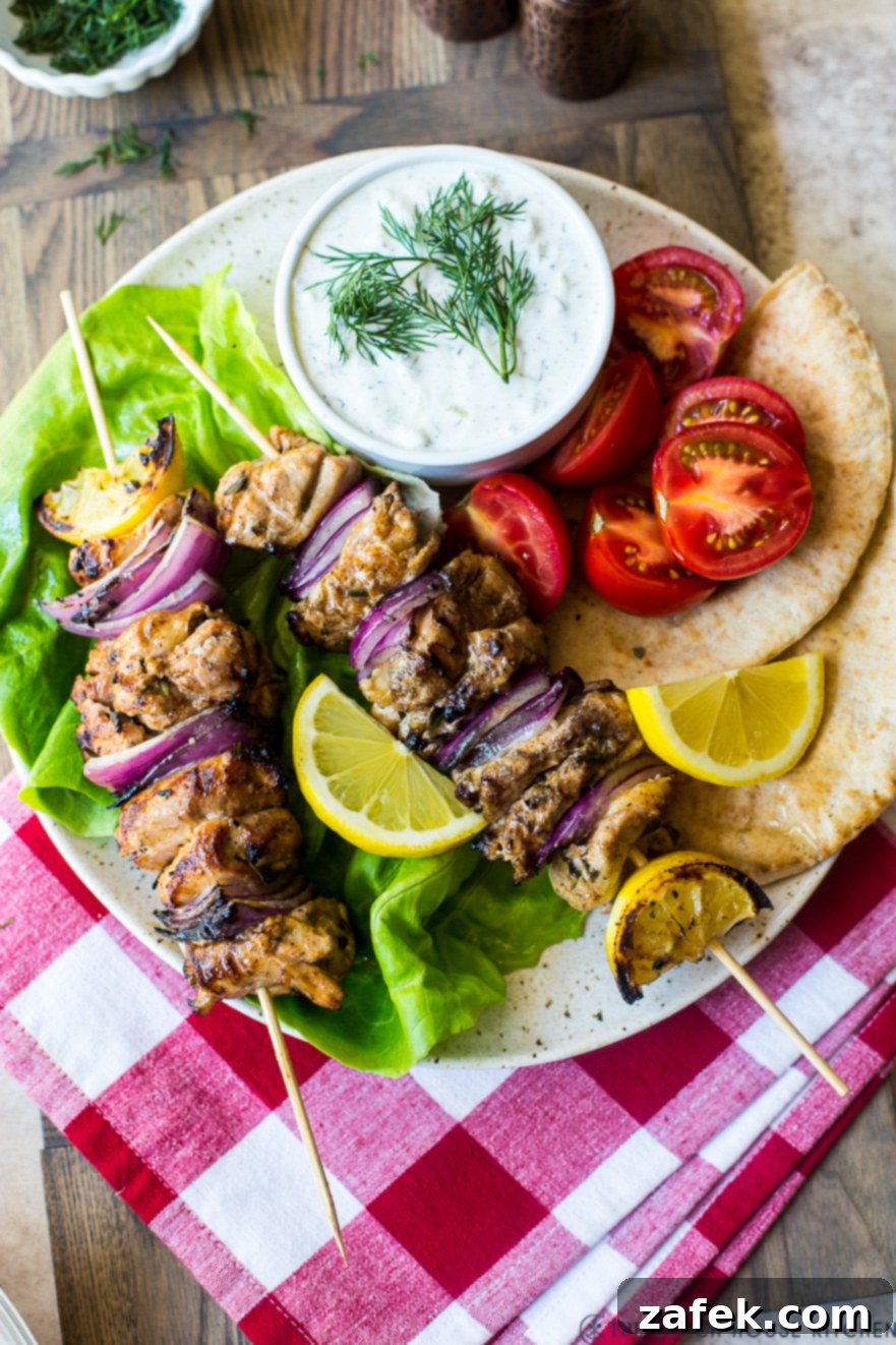 Overhead photo of Chicken Souvlaki Skewers with Tzatziki Sauce on a plate on top of a red and white checked napkin.