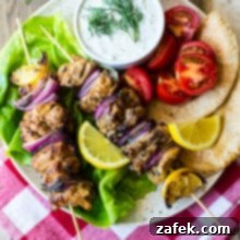 Overhead photo of Chicken Souvlaki Skewers with Tzatziki Sauce on a plate on top of a red and white checked napkin.