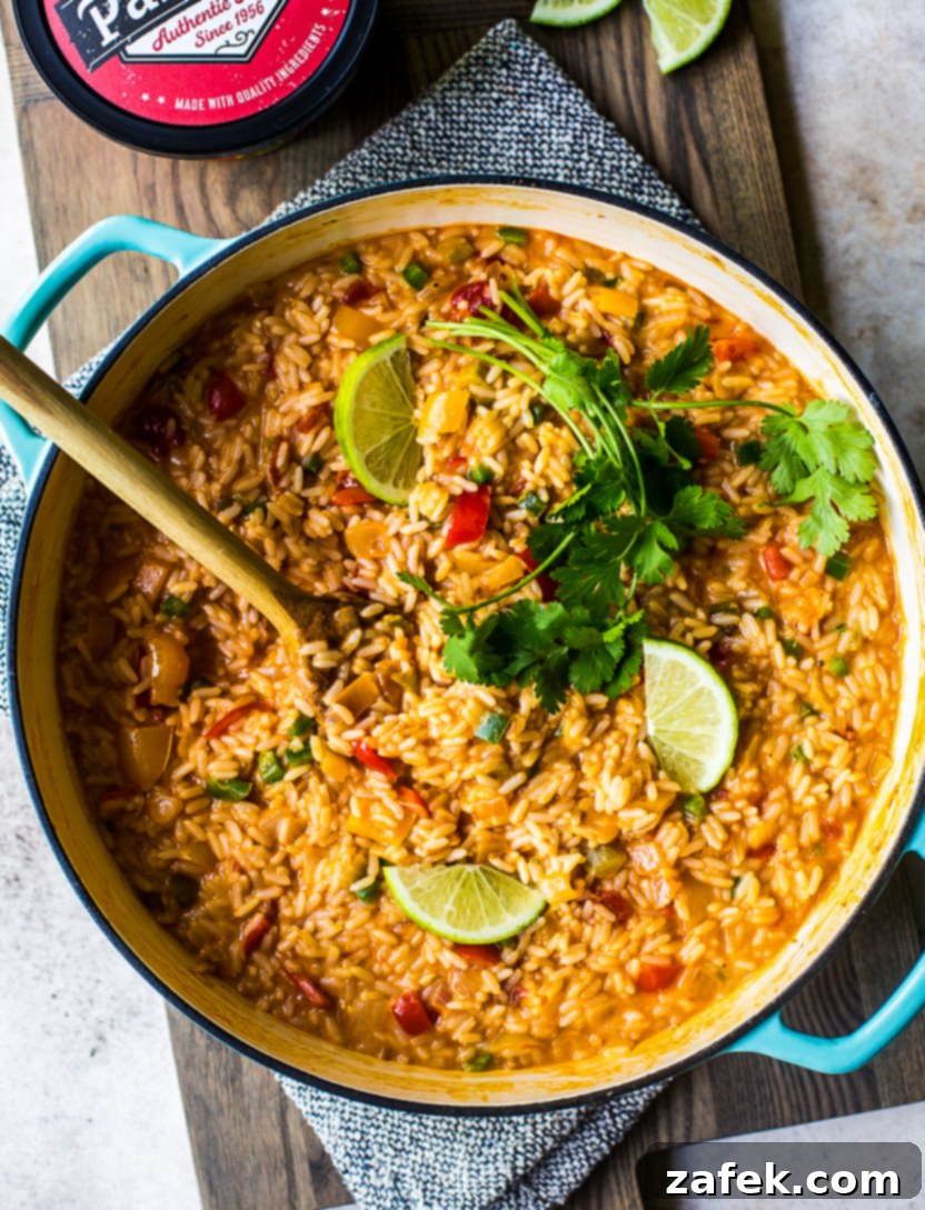 Overhead photo of a baking dish of cheesy queso fiesta rice topped with fresh cilantro and vibrant lime slices, ready to be served